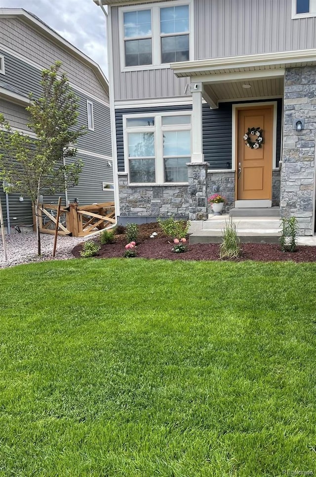 doorway to property featuring board and batten siding, stone siding, and a lawn