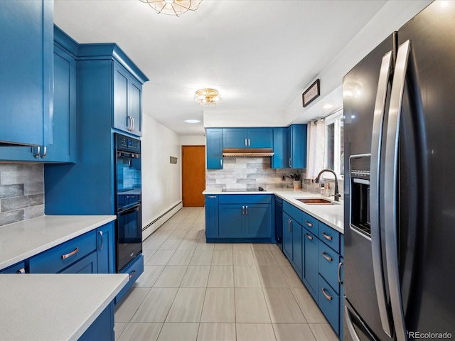 kitchen with baseboard heating, black appliances, blue cabinetry, decorative backsplash, and sink