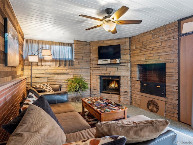 living room featuring ceiling fan, a stone fireplace, wooden ceiling, and carpet