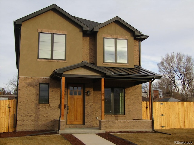 view of front of property with a standing seam roof, brick siding, fence, and stucco siding