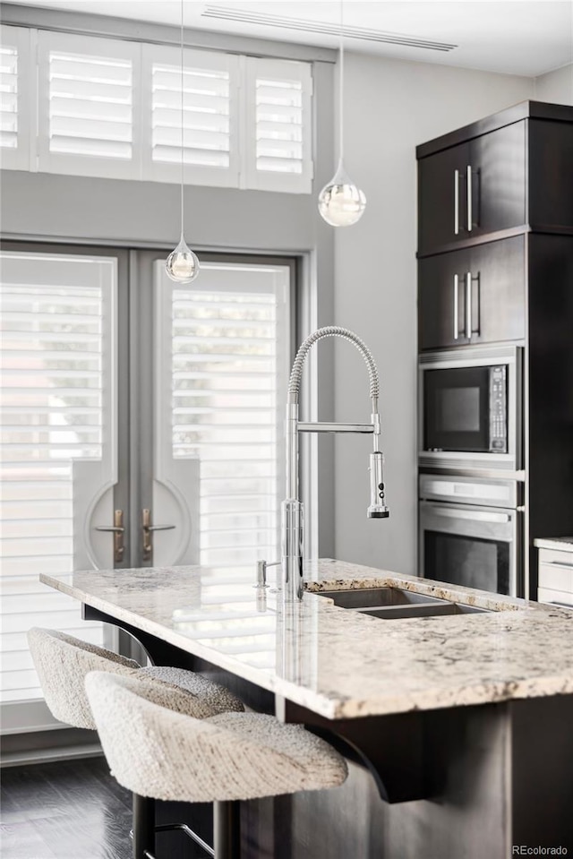 kitchen featuring black microwave, hardwood / wood-style floors, stainless steel oven, and light stone counters