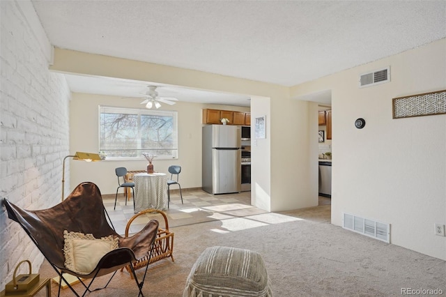 sitting room featuring a textured ceiling, light colored carpet, ceiling fan, and brick wall