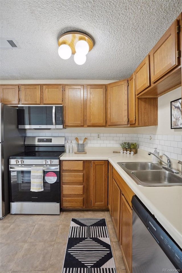 kitchen with tasteful backsplash, a textured ceiling, stainless steel appliances, sink, and light tile patterned flooring