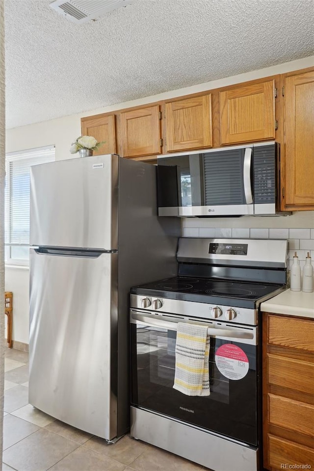 kitchen featuring tasteful backsplash, light tile patterned flooring, stainless steel appliances, and a textured ceiling