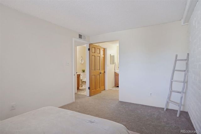 bedroom featuring ensuite bath, light colored carpet, and a textured ceiling