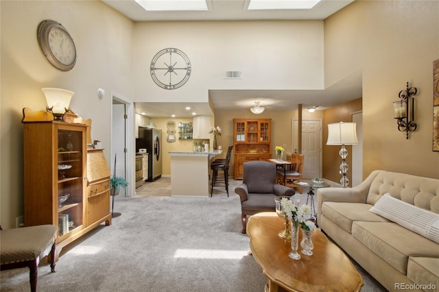 living area featuring a towering ceiling, light carpet, a skylight, and baseboards