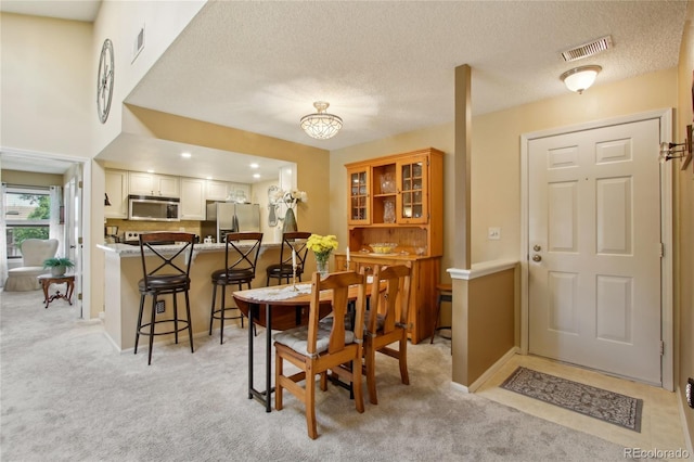 dining area with light colored carpet, a textured ceiling, and baseboards