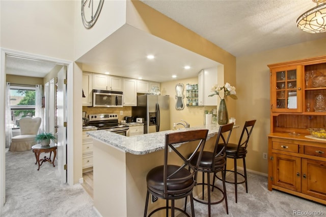 kitchen featuring appliances with stainless steel finishes, light colored carpet, a peninsula, a kitchen breakfast bar, and light stone counters