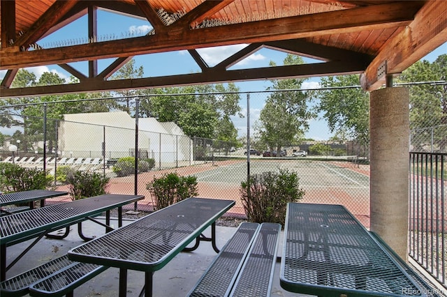 view of patio / terrace with a tennis court, fence, and outdoor dining space