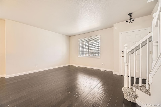 unfurnished living room featuring dark wood finished floors, a textured ceiling, stairs, and baseboards