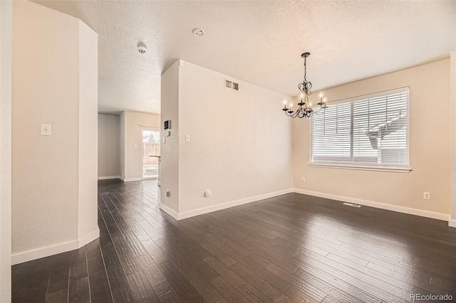 unfurnished room with visible vents, dark wood-type flooring, baseboards, an inviting chandelier, and a textured ceiling