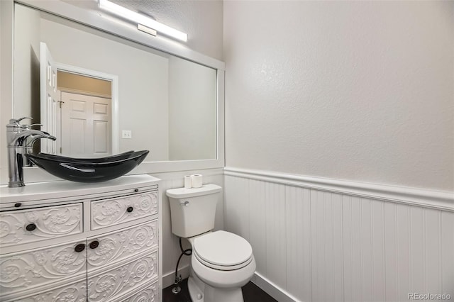 half bath with vanity, toilet, and a wainscoted wall