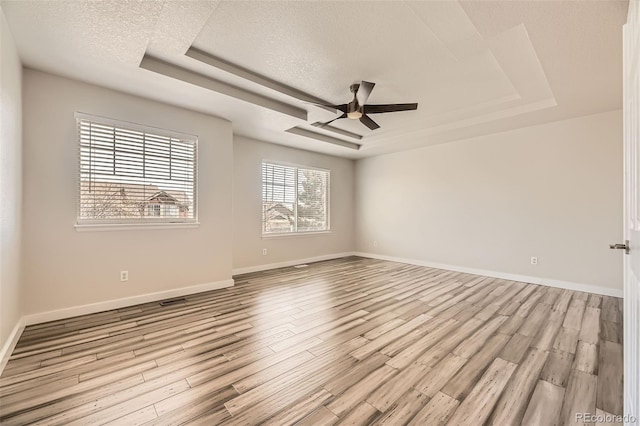 spare room with light wood-type flooring, a tray ceiling, a textured ceiling, baseboards, and ceiling fan