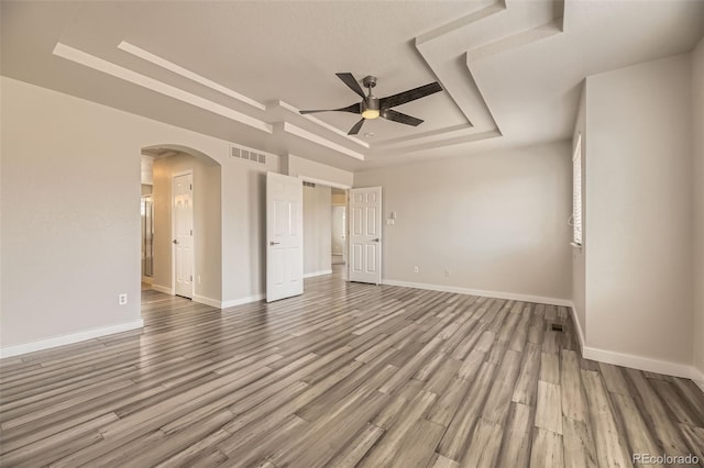 unfurnished room with visible vents, baseboards, a tray ceiling, wood finished floors, and arched walkways