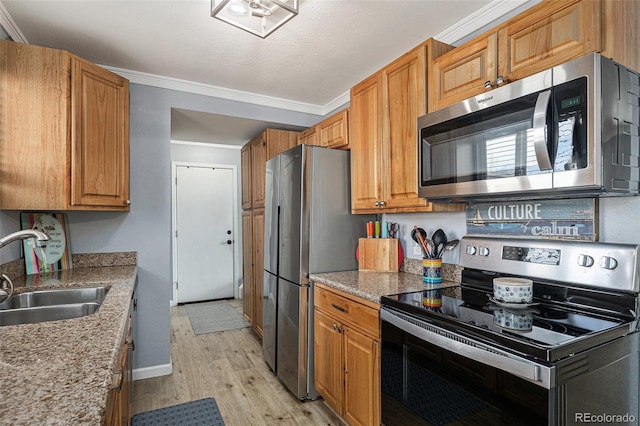 kitchen with light wood-style flooring, a sink, ornamental molding, appliances with stainless steel finishes, and light stone countertops