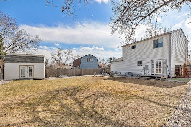 back of property featuring french doors, a lawn, an outdoor structure, and a fenced backyard