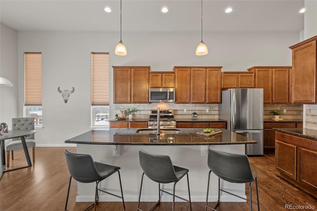 kitchen with stainless steel appliances, hanging light fixtures, a kitchen island with sink, and tasteful backsplash