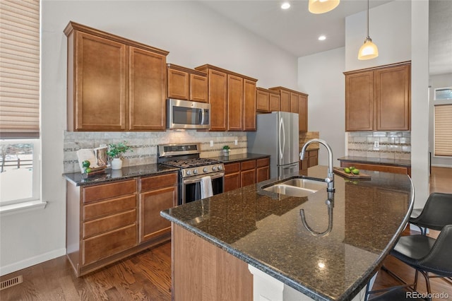 kitchen featuring dark stone counters, hanging light fixtures, sink, an island with sink, and stainless steel appliances