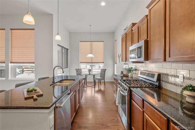 kitchen featuring decorative backsplash, sink, pendant lighting, stainless steel appliances, and a center island with sink