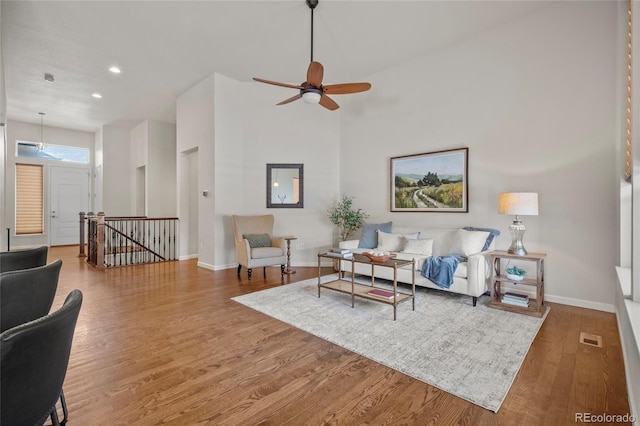 living room with ceiling fan, hardwood / wood-style floors, and a towering ceiling