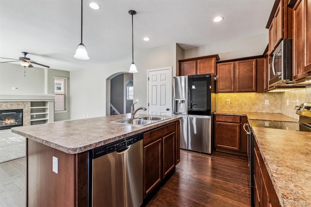 kitchen with appliances with stainless steel finishes, pendant lighting, sink, dark hardwood / wood-style flooring, and a center island with sink