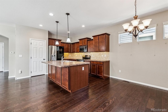 kitchen with tasteful backsplash, stainless steel appliances, decorative light fixtures, and a center island with sink