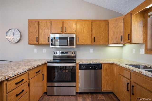 kitchen with appliances with stainless steel finishes, dark hardwood / wood-style flooring, light stone counters, a textured ceiling, and lofted ceiling