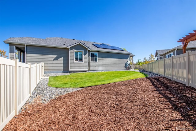 rear view of property with solar panels and a lawn