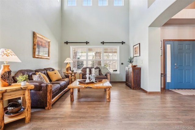 living area with arched walkways, a towering ceiling, baseboards, and wood finished floors