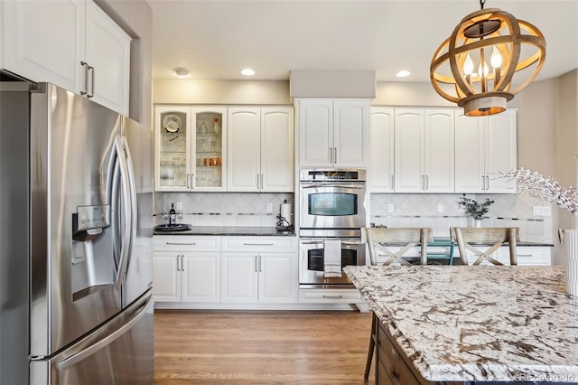 kitchen featuring decorative light fixtures, stainless steel appliances, tasteful backsplash, light wood-style floors, and white cabinetry