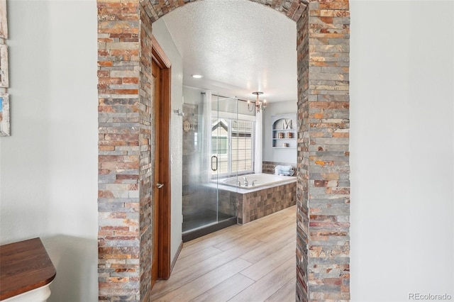 bathroom with wood finish floors, a garden tub, an inviting chandelier, a textured ceiling, and a shower stall