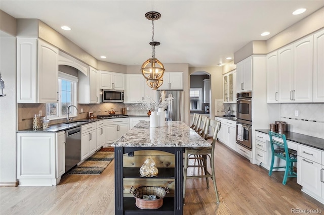 kitchen featuring appliances with stainless steel finishes, arched walkways, a sink, and light wood finished floors