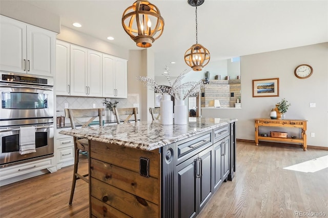 kitchen with light wood finished floors, stainless steel double oven, white cabinetry, and tasteful backsplash