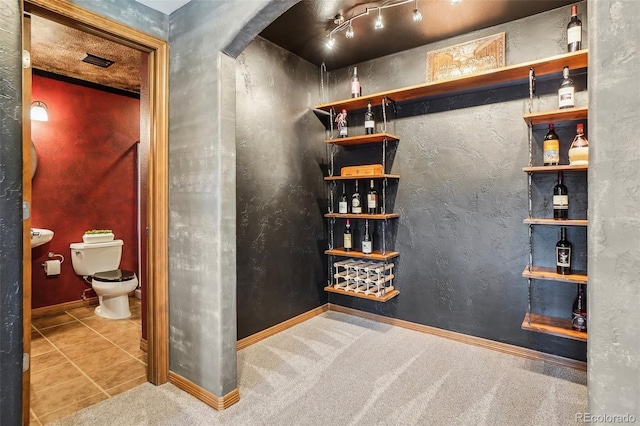 wine area featuring a dry bar, tile patterned flooring, carpet flooring, and baseboards