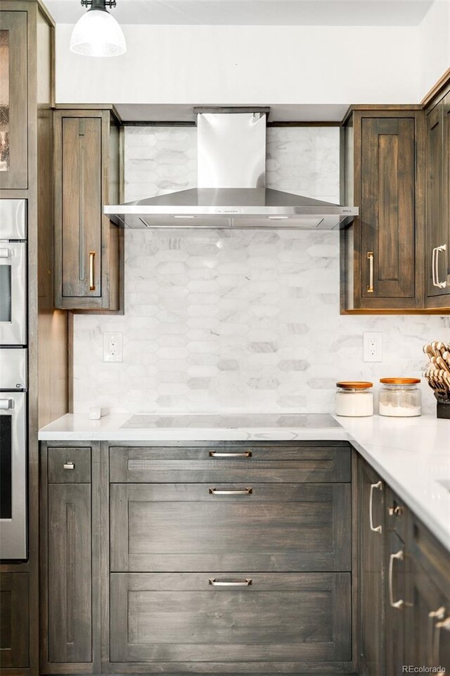 1551 Larimer St Unit 1405, Denver, CO 80202 - kitchen featuring cooktop, light countertops, dark brown cabinets, wall chimney range hood, and backsplash