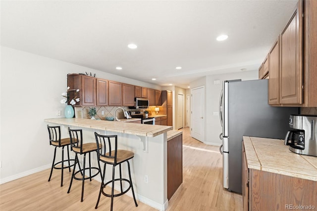 kitchen featuring tile counters, light hardwood / wood-style flooring, kitchen peninsula, a breakfast bar area, and appliances with stainless steel finishes