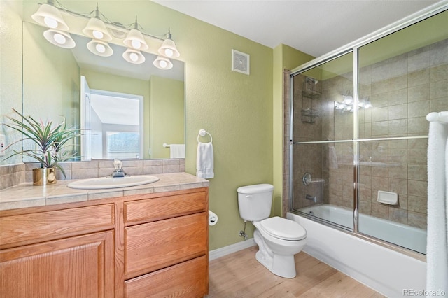 full bathroom featuring hardwood / wood-style floors, vanity, toilet, and bath / shower combo with glass door