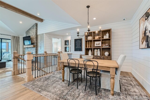 dining room with wood walls, a chandelier, vaulted ceiling with beams, and light hardwood / wood-style flooring