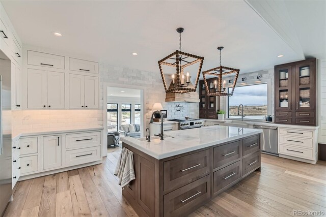 kitchen with stainless steel appliances, decorative light fixtures, white cabinetry, backsplash, and a center island with sink