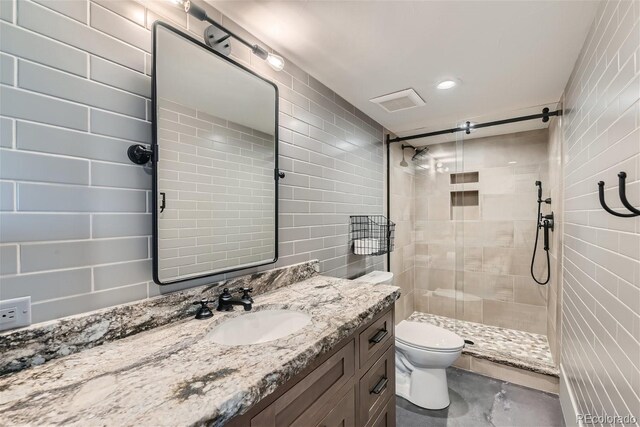 bathroom with toilet, tiled shower, and vanity