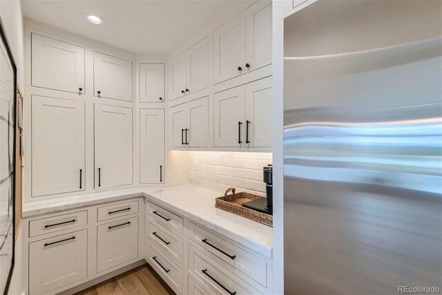 kitchen with white cabinetry, stainless steel refrigerator, light stone counters, light hardwood / wood-style flooring, and backsplash