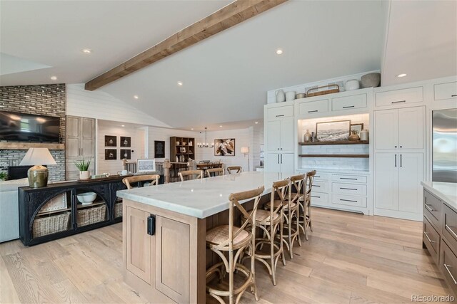 kitchen featuring a spacious island, a kitchen bar, white cabinetry, built in refrigerator, and vaulted ceiling with beams