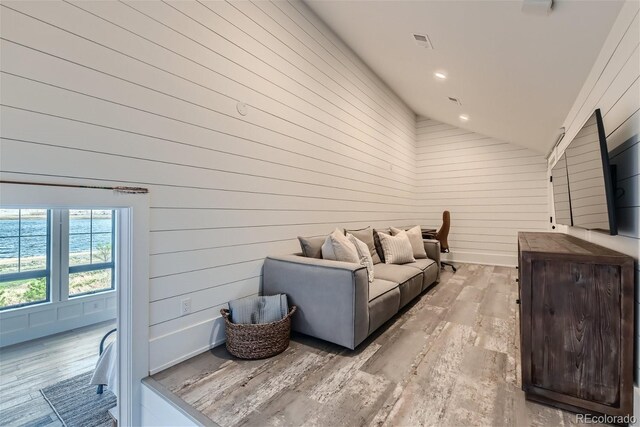 living room featuring vaulted ceiling, light hardwood / wood-style flooring, and wooden walls