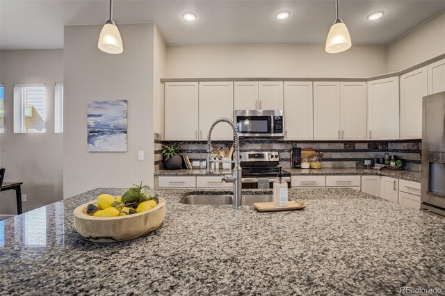 1341 Solitaire St, Colorado Springs, CO 80905 - kitchen with decorative light fixtures, stainless steel appliances, dark stone countertops, decorative backsplash, and a sink