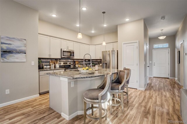 1341 Solitaire St, Colorado Springs, CO 80905 - kitchen with light wood-type flooring, a center island with sink, a sink, light stone countertops, and appliances with stainless steel finishes