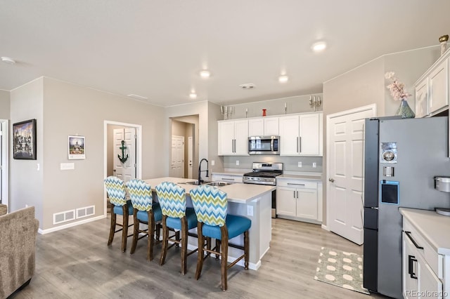 kitchen with white cabinetry, appliances with stainless steel finishes, light hardwood / wood-style flooring, and a center island with sink