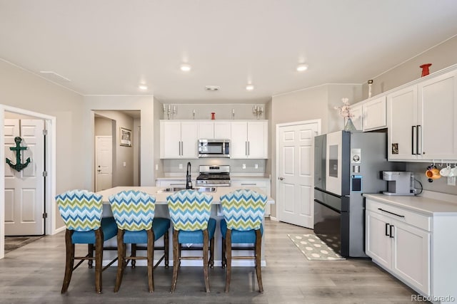 kitchen with appliances with stainless steel finishes, sink, wood-type flooring, white cabinets, and a center island with sink