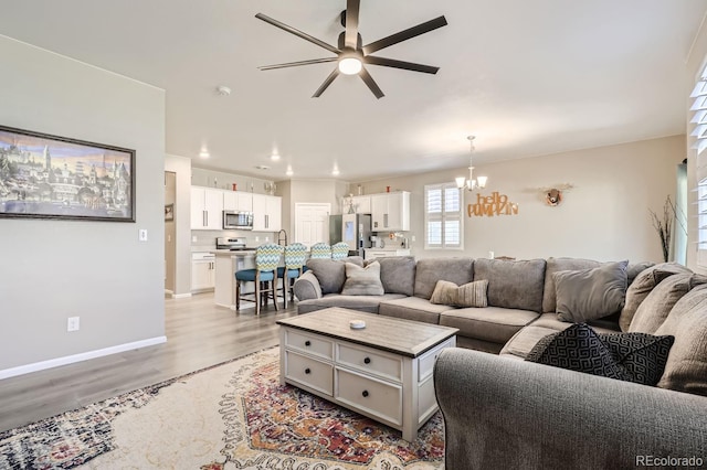 living room with ceiling fan with notable chandelier and light hardwood / wood-style floors