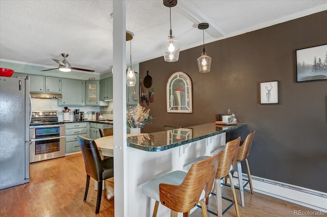 kitchen with light wood finished floors, stainless steel appliances, green cabinetry, baseboard heating, and under cabinet range hood