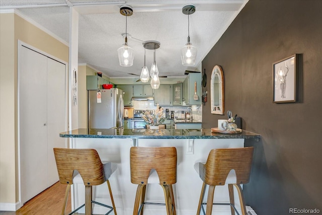 kitchen featuring crown molding, wood finished floors, a textured ceiling, green cabinets, and stainless steel appliances